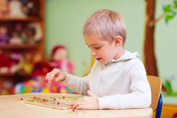 Leuke jongen, kind met speciale behoeften oplossen van een puzzel in revalidatiecentrum — Stockfoto