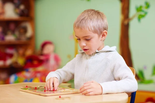 Garçon mignon, enfant avec des besoins spéciaux résoudre un puzzle dans le centre de réadaptation — Photo
