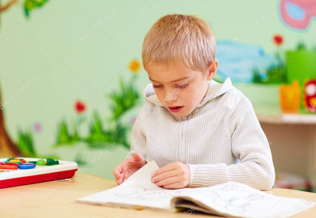 cute boy, kid with special needs looking at a book, in rehabilitation center
