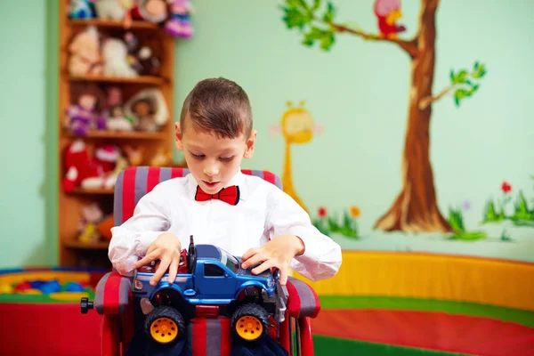 Schattige gelukkige jongen op rolstoel met heden in de kleuterschool voor kinderen met speciale behoeften — Stockfoto