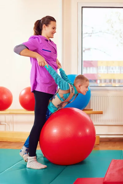 Lindo niño con discapacidad tiene terapia musculoesquelética haciendo ejercicios en cinturones de fijación del cuerpo en la bola en forma — Foto de Stock