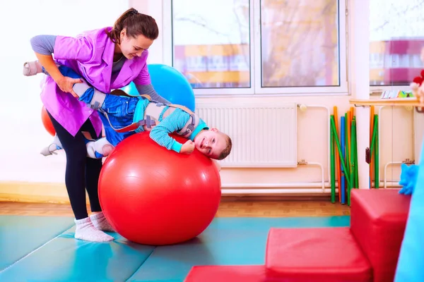 Enfant mignon avec handicap a une thérapie musculo-squelettique en faisant des exercices dans les ceintures de fixation du corps sur la balle en forme — Photo