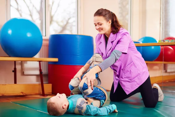 Lindo niño con discapacidad tiene terapia musculoesquelética haciendo ejercicios en cinturones de fijación del cuerpo —  Fotos de Stock