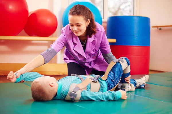 Cute kid with disability has musculoskeletal therapy by doing exercises in body fixing belts — Stock Photo, Image