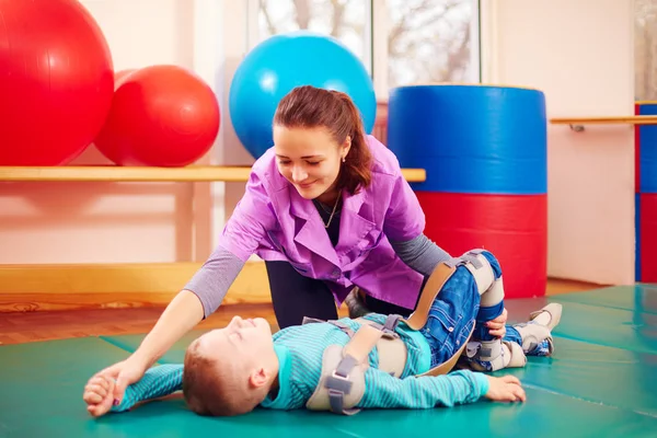 Cute kid with disability has musculoskeletal therapy by doing exercises in body fixing belts — Stock Photo, Image