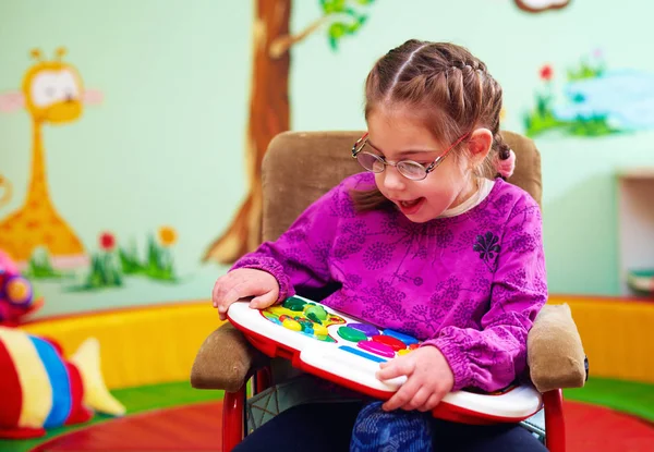 Милая девочка в инвалидной коляске играет с развивающейся игрушкой в детском саду для детей с особыми потребностями — стоковое фото