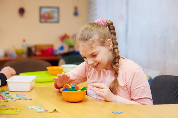 Linda chica feliz con discapacidad desarrolla las habilidades motoras finas en el centro de rehabilitación para niños con necesidades especiales —  Fotos de Stock