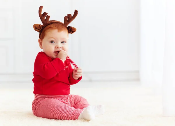 Cute redhead baby eating christmas candy at home — Stock Photo, Image