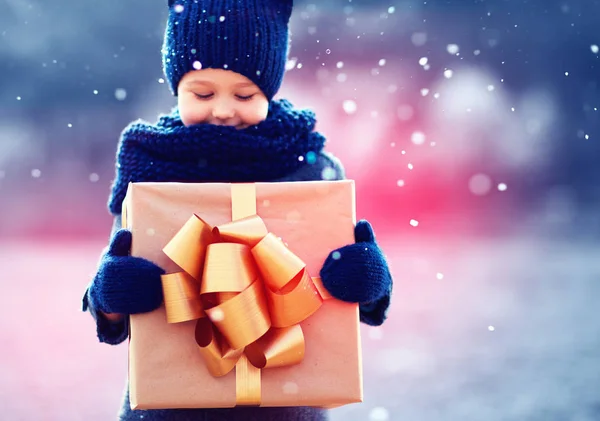 Happy kid with big gift box under a snowfall. Focus on gift box — Stock Photo, Image