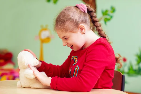 Мила дівчинка грає з плюшевою іграшкою в дитячому садку для дітей з особливою потребою — стокове фото