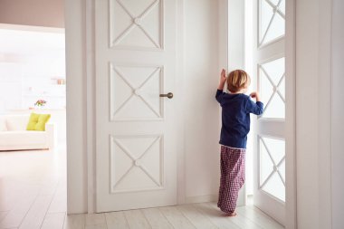 curious young boy looks into the ajar door clipart