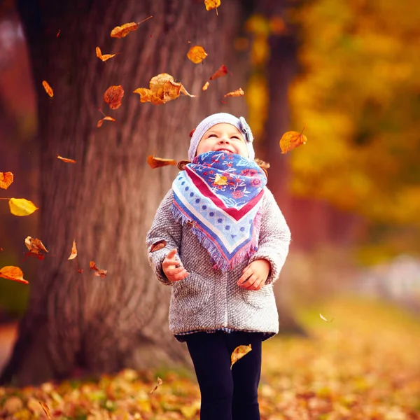 Hermosa niña feliz divirtiéndose en el parque de otoño, entre hojas caídas —  Fotos de Stock