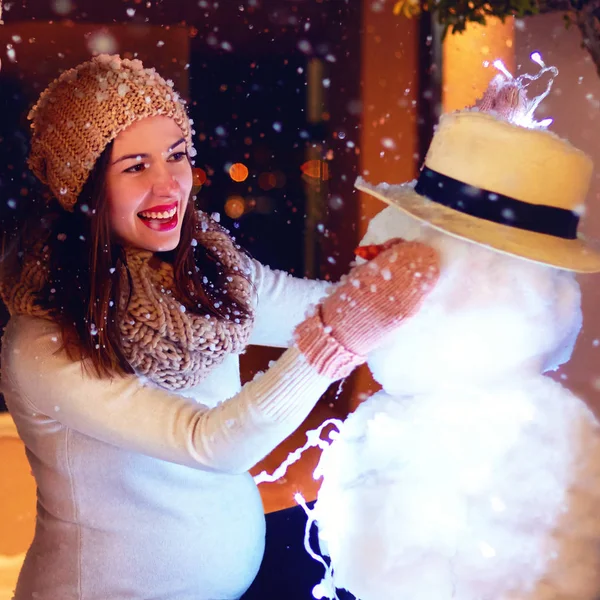 Piękna kobieta w ciąży szczęśliwy Dokonywanie bałwana w magiczny zima śnieg — Zdjęcie stockowe