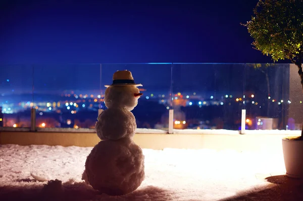 Muñeco de nieve lindo en la terraza de la azotea, fondo de la ciudad —  Fotos de Stock