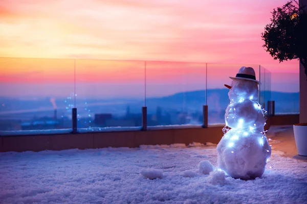 Lindo muñeco de nieve viendo el sol se pone en la terraza de la azotea —  Fotos de Stock