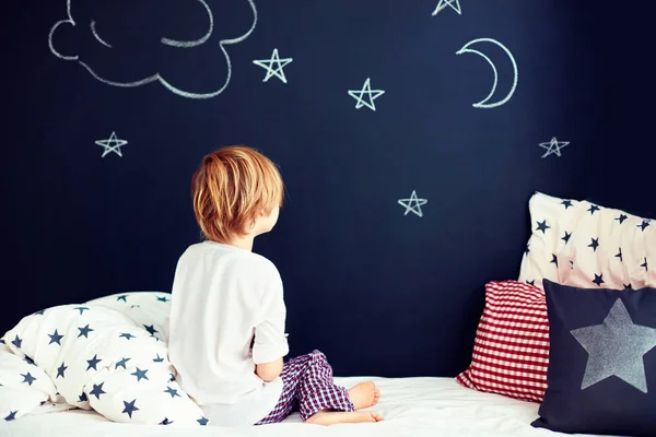 Garoto bonito em pijama sonhando, enquanto sentado na cama — Fotografia de Stock
