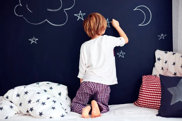 Cute kid in pajamas painting chalkboard wall in his bedroom — Stock Photo, Image