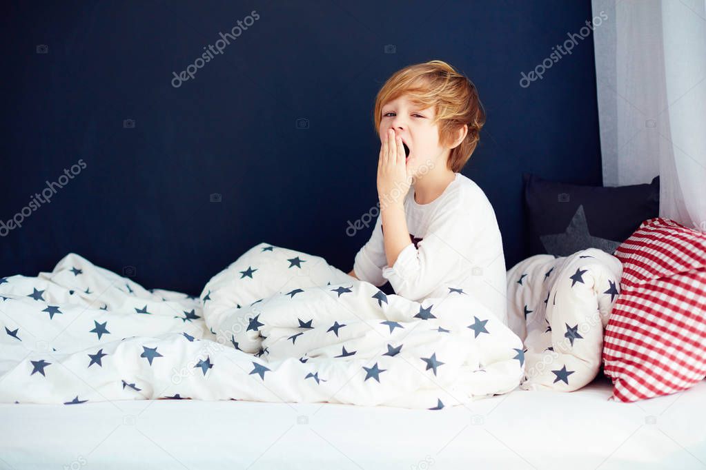 cute yawning kid in pajamas sitting in bed
