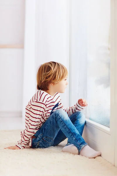Przystojny, młody chłopak siedzi na dywanie w pobliżu okna w domu — Zdjęcie stockowe