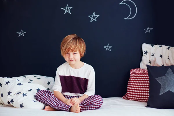 Милый улыбающийся ребенок в пижаме сидит на кровати в детской комнате — стоковое фото