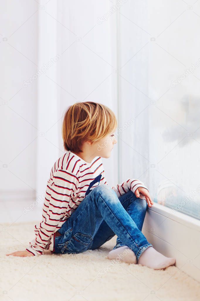 handsome young boy sitting on carpet near the window at rainy day