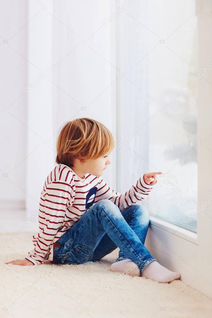 handsome young boy sitting on carpet near the window at rainy day