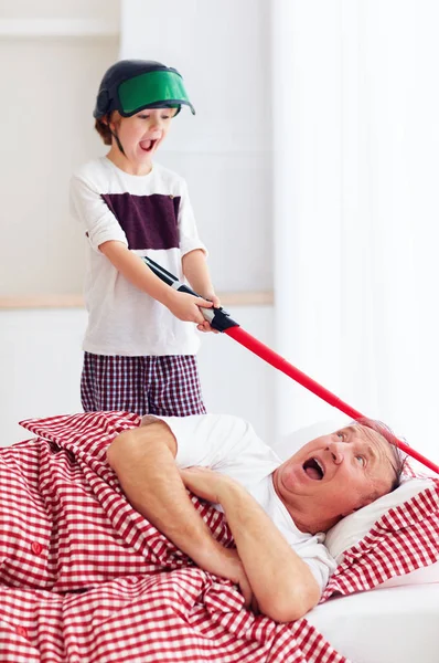 Naughty yelling grandson waking grandpa up by playing around in loud, noisy games — Stock Photo, Image