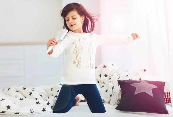 Cute happy girl singing into the microphone brush in the morning sun light at home — Stock Photo, Image