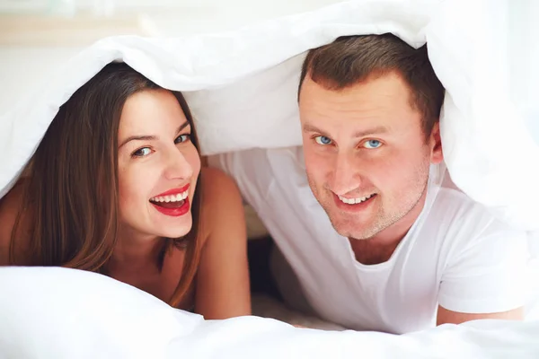 Happy couple playing under duvet cover at bedroom — Stock Photo, Image