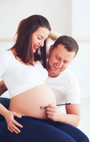 Lyckligt par skriva ett namn på en bebis på gravid mage — Stockfoto