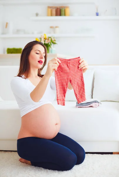 Gravid kvinna inför hennes nya bebis hemma kläder — Stockfoto