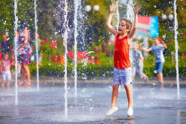 Aufgeregter Junge, der sich zwischen Wasserstrahlen im Springbrunnen vergnügt. Sommer in der Stadt — Stockfoto