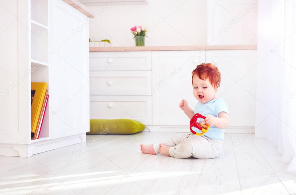 cute ginger baby boy playing with toys in bright kitchen, at home