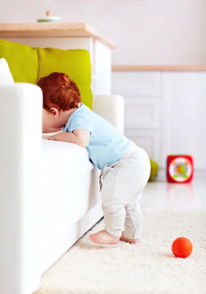 Menino de gengibre infantil bonito tentando subir o sofá em casa — Fotografia de Stock