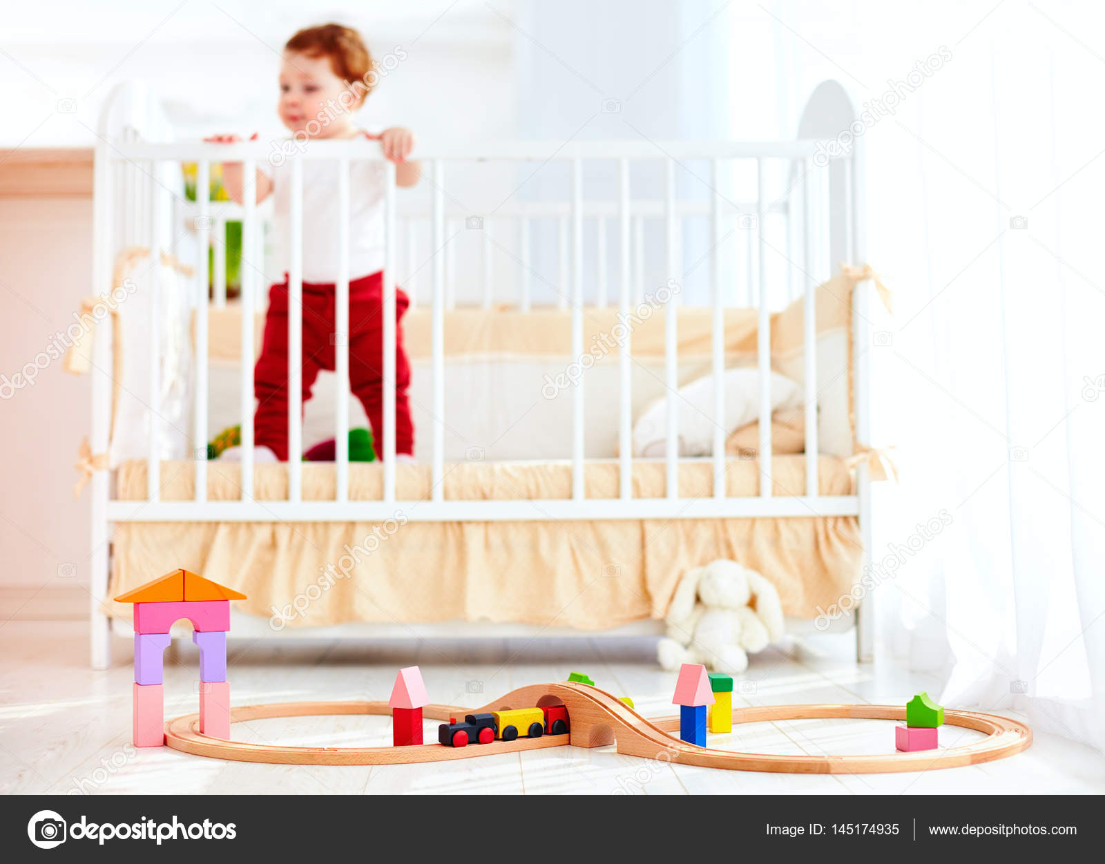 Toys on the floor in sunny bedroom with infant baby in the crib on