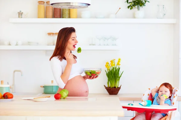 Młoda matka w ciąży i niemowląt baby w krzesełko obiedzie na kuchnia w domu — Zdjęcie stockowe