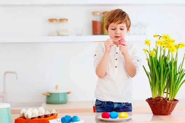 Lindo niño feliz pintura huevos de Pascua en el escritorio de la cocina — Foto de Stock