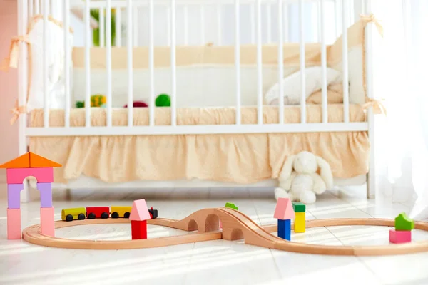 Brinquedos no chão em ensolarado quarto de bebê com berço no fundo — Fotografia de Stock