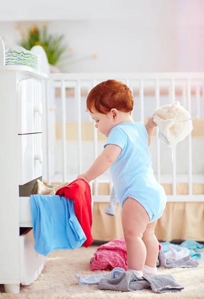 Funny infant baby throwing out clothes from the dresser at home — Stock Photo, Image