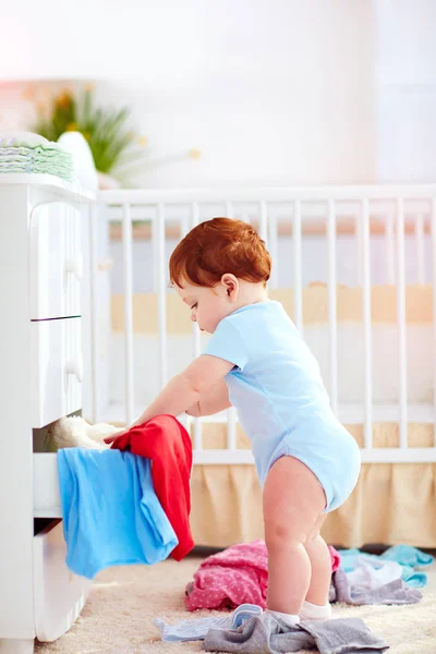 Смешной младенец выбрасывает одежду из шкафа дома — стоковое фото