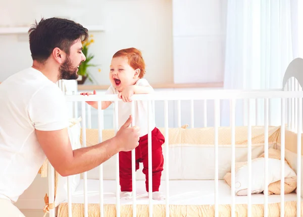 Счастливый отец играет с младенцем в детской кроватке дома — стоковое фото