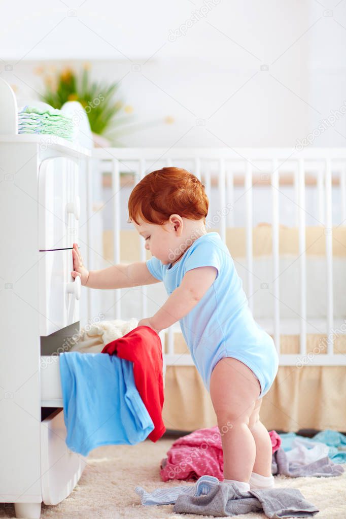 funny infant baby throwing out clothes from the dresser at home