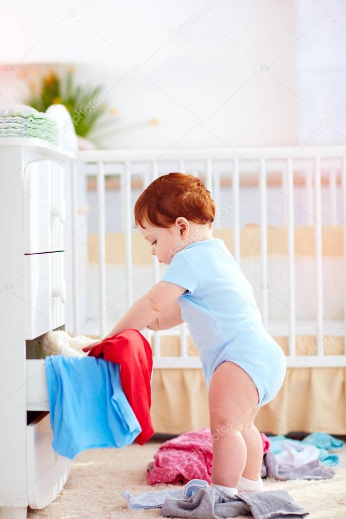 funny infant baby throwing out clothes from the dresser at home