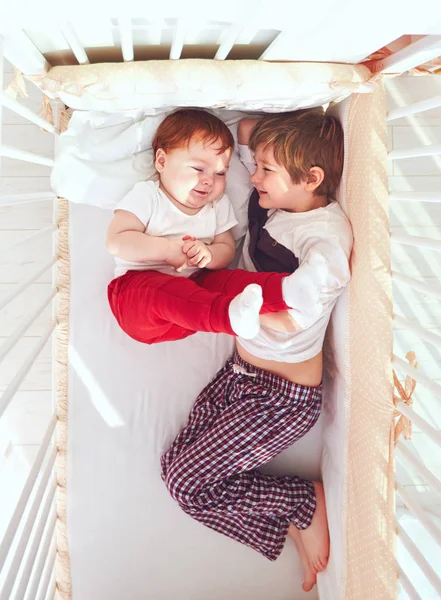 Веселые братья веселятся, лежа в кроватке вместе — стоковое фото