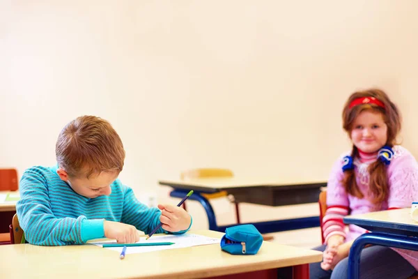 Mignon garçon avec des besoins spéciaux écrire des lettres tout en étant assis au bureau dans la salle de classe — Photo