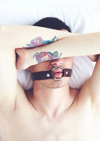 Young man with tattoo and face strap laying in bed — Stock Photo, Image