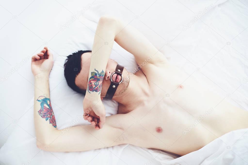 young man with tattoo and face strap laying in bed in the morning
