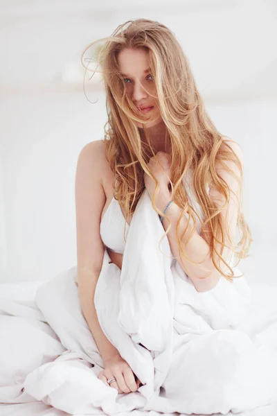 Young sensual woman with wild hair sitting on bed in white sheets — Stock Photo, Image