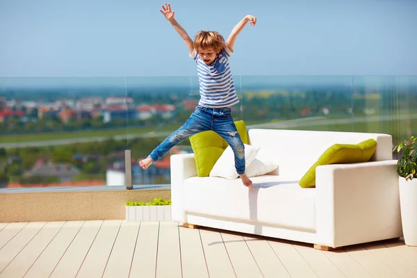 Niño feliz, niño saltando desde el sofá en la terraza de la azotea en un día cálido y soleado — Foto de Stock