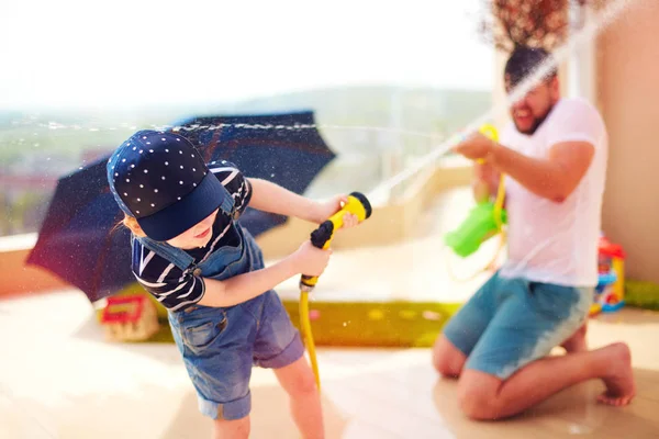 Excited young boy having fun, splashing water with father at warm summer day — Stock Photo, Image